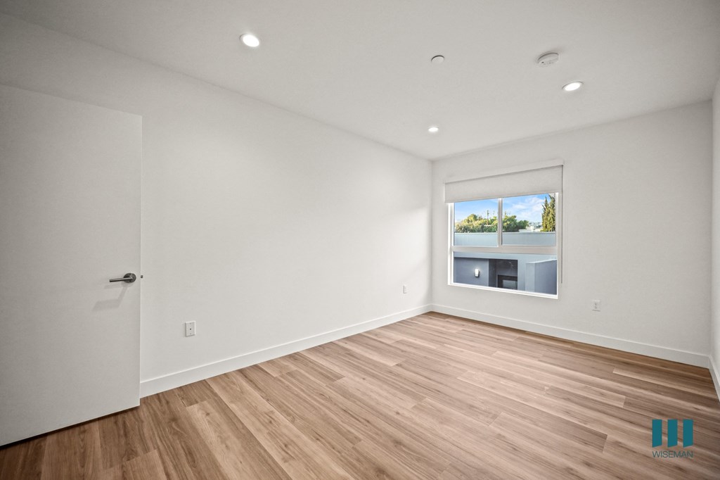 A room with a white door and a window showing a view of a building and trees.