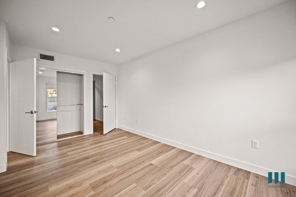 A room with wooden floors and white walls, with a door on the left and two open doors on the right.
