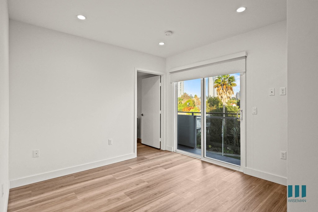 A room with a sliding glass door leading to a balcony with a view of trees.