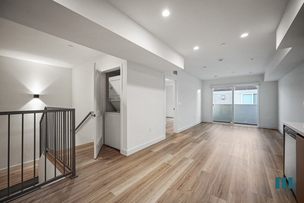 A spacious room with wooden floors and a staircase with a metal railing.
