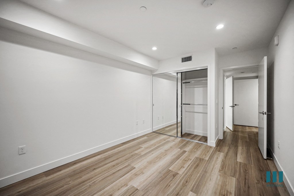 A room with white walls and wood flooring with a door on the right.