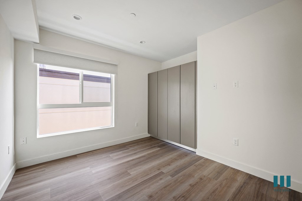 a bedroom with white walls and wood floors and a window