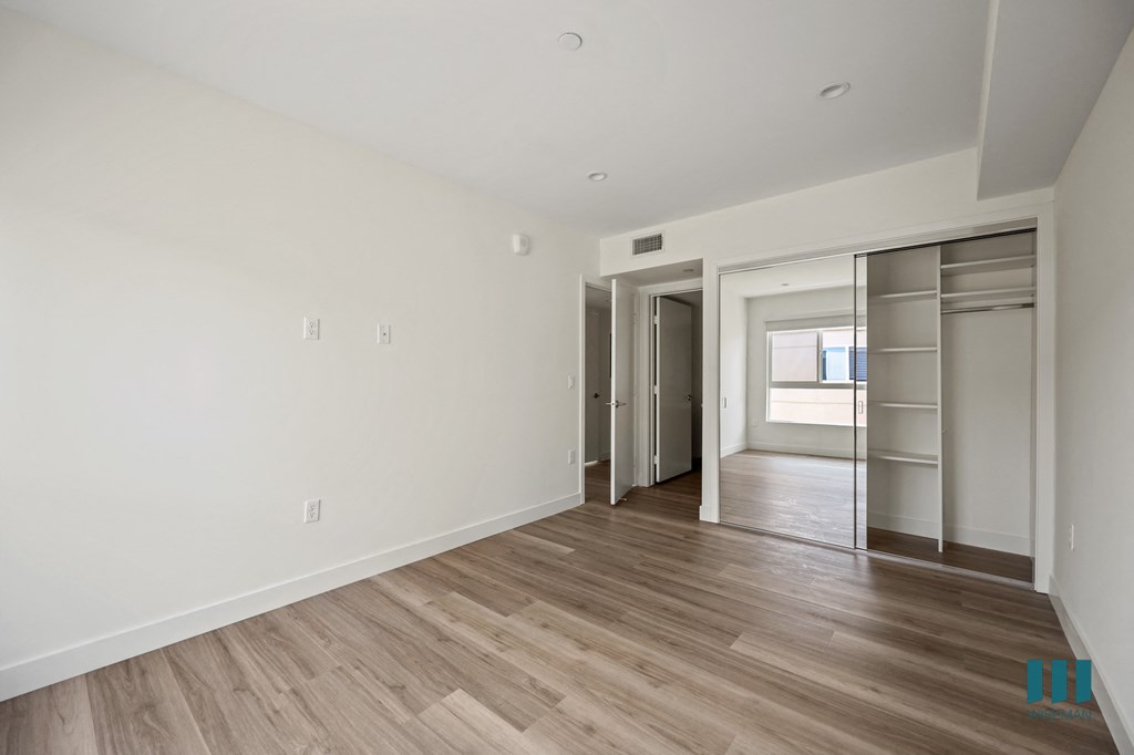 a bedroom with white walls and wood flooring and a closet