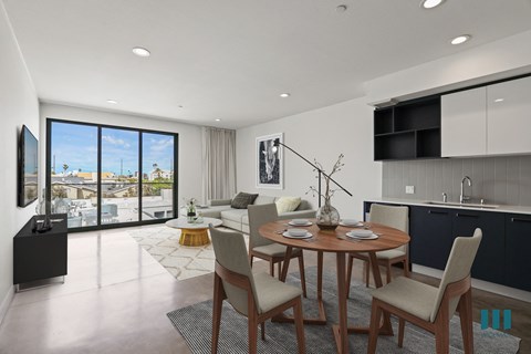 a living area with a table and chairs and a kitchen with a large window