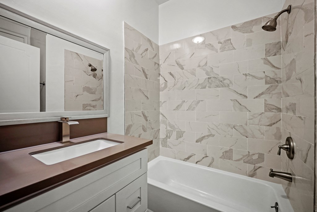 A bathroom with a marble tile wall and a white bathtub.