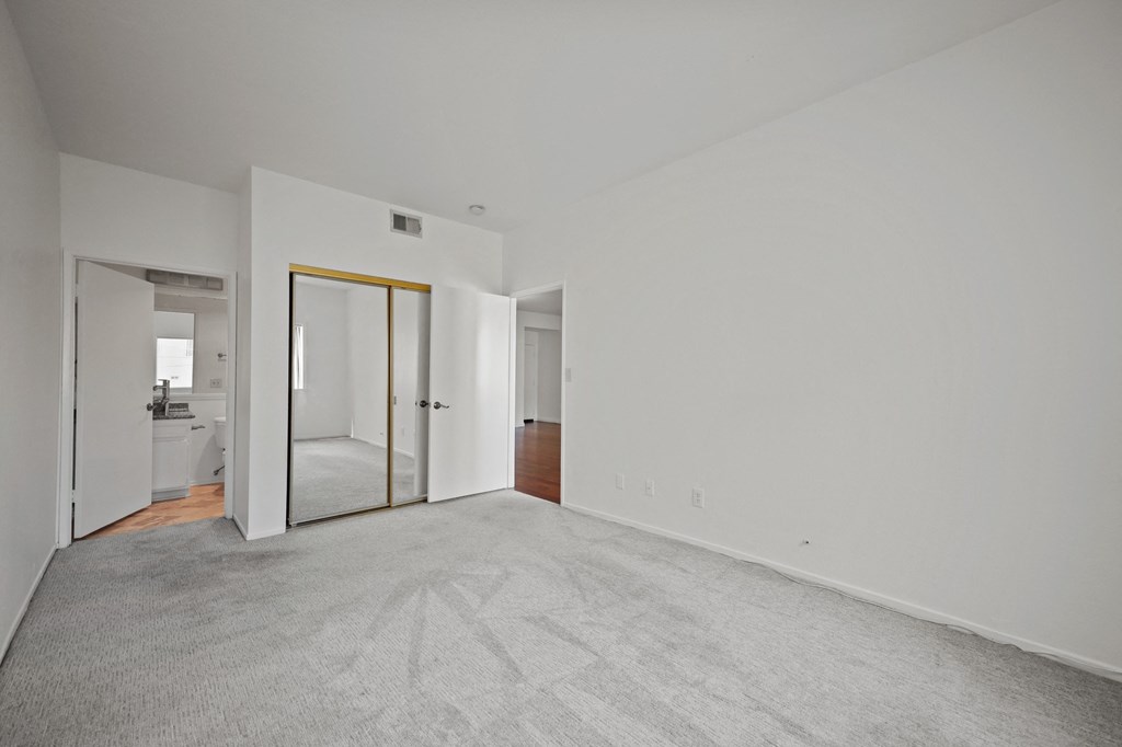 an empty living room with white walls and a mirror in the corner