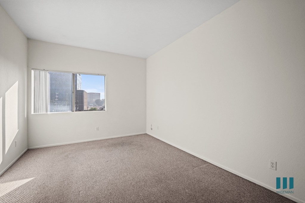 A large empty room with a carpeted floor and a window.