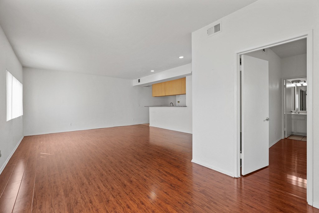 an empty living room and kitchen with wood floors and white walls