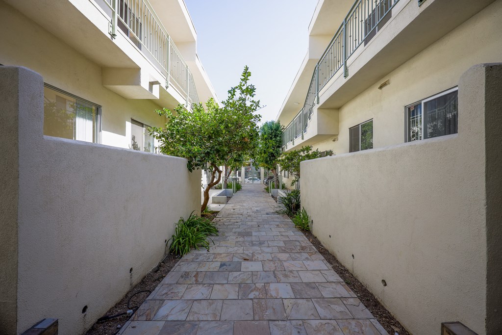 the walkway between the apartments is lined with trees and plants