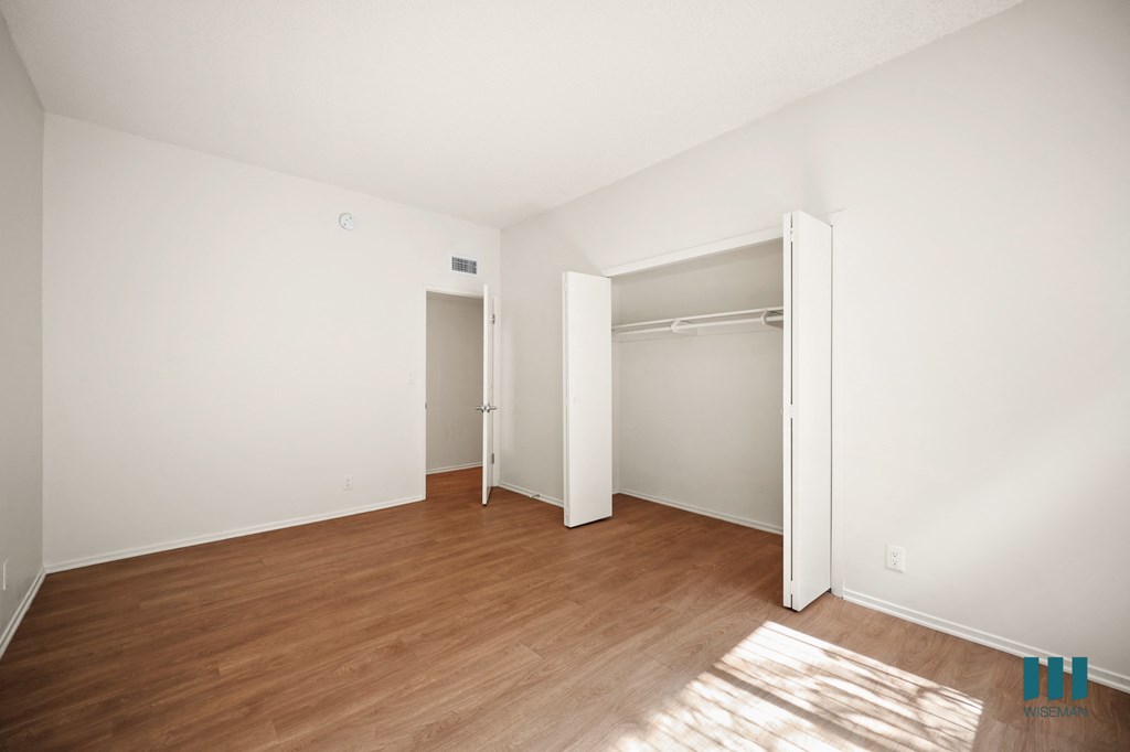 a bedroom with white walls and wood flooring and a closet