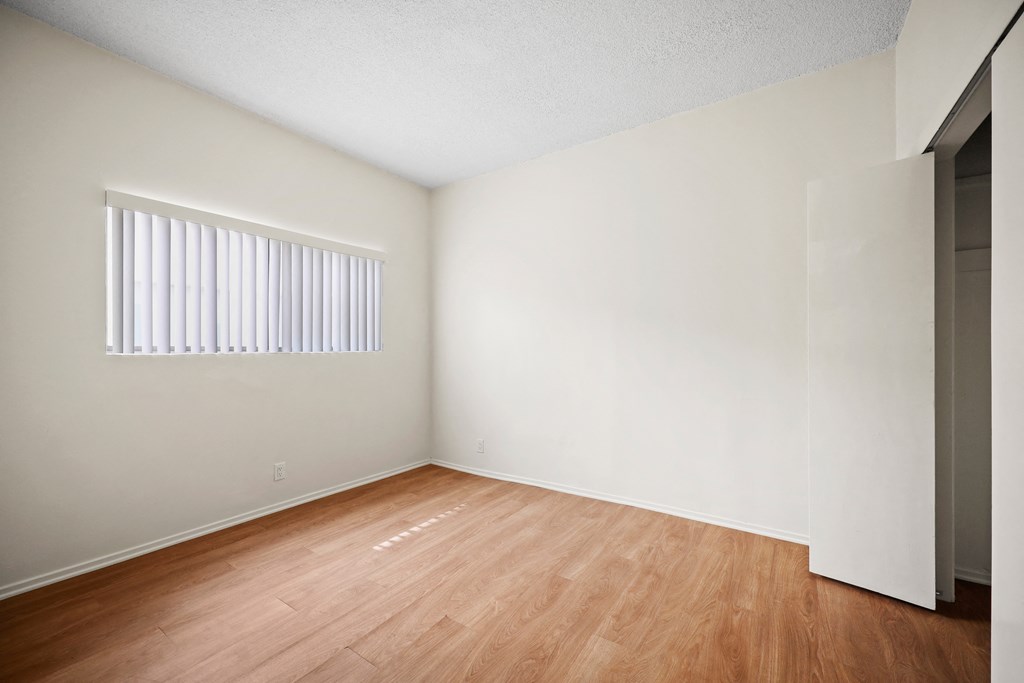 the spacious living room of an apartment with wood flooring and a window
