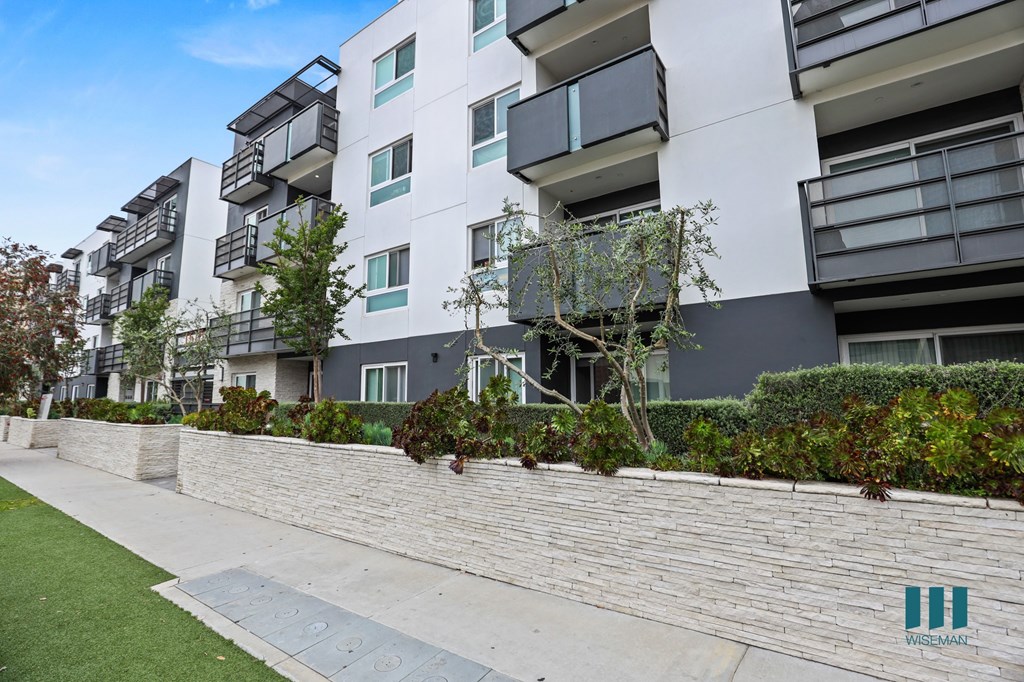 A modern apartment building with a stone wall and greenery in front.