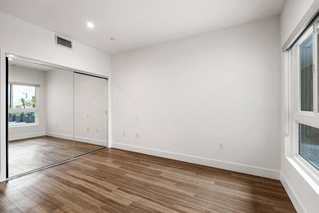 Bedroom with Mirrored Closet, Large Windows, and Vinyl Flooring