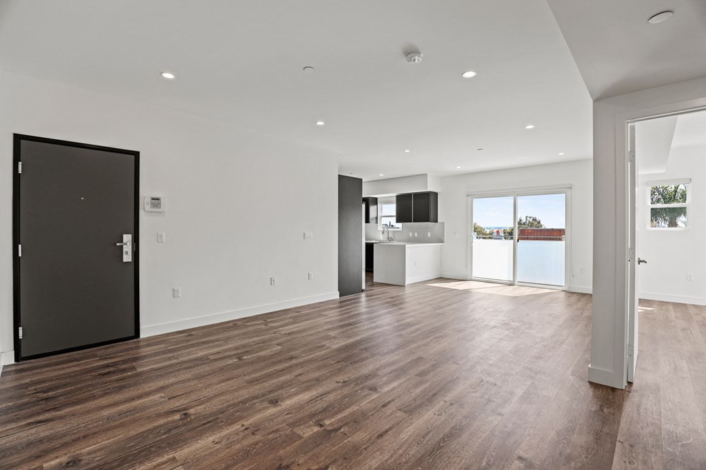 a living room and kitchen in a house with white walls and a wooden floor