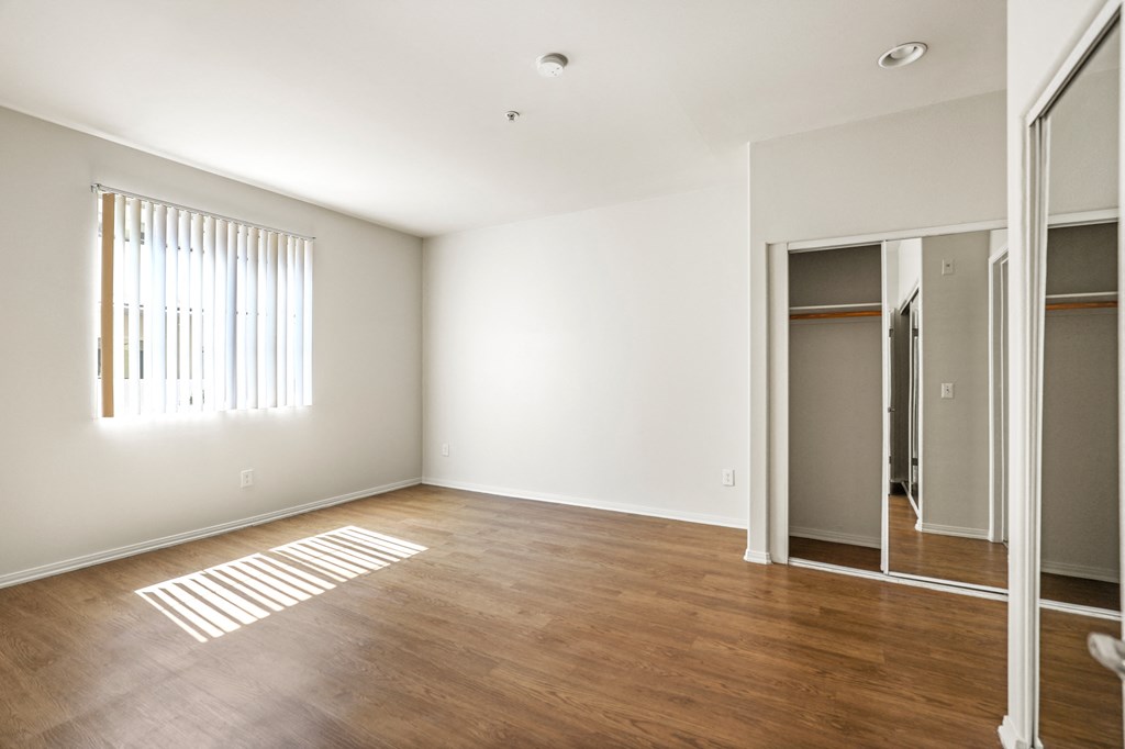 Spacious Bedroom with Mirrored Closet, Window, and Vinyl Flooring