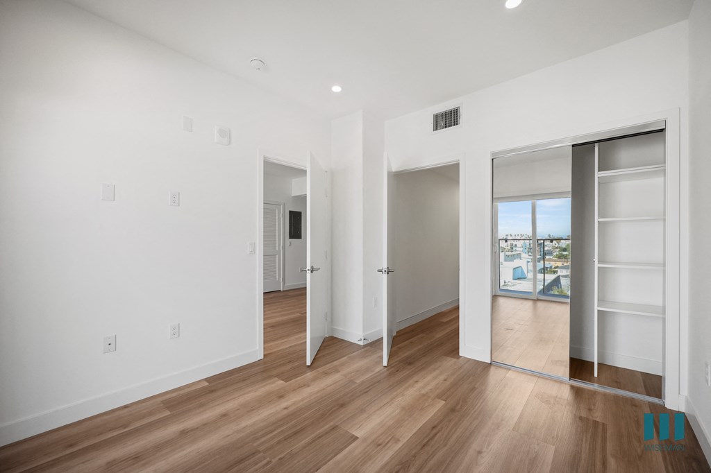 A room with white walls and wooden flooring, with a doorway leading to another room.