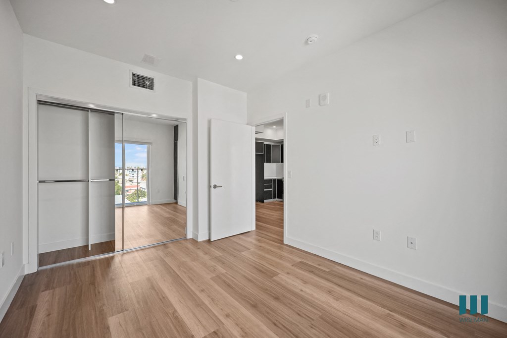 A room with white walls and wooden flooring with a sliding glass door.