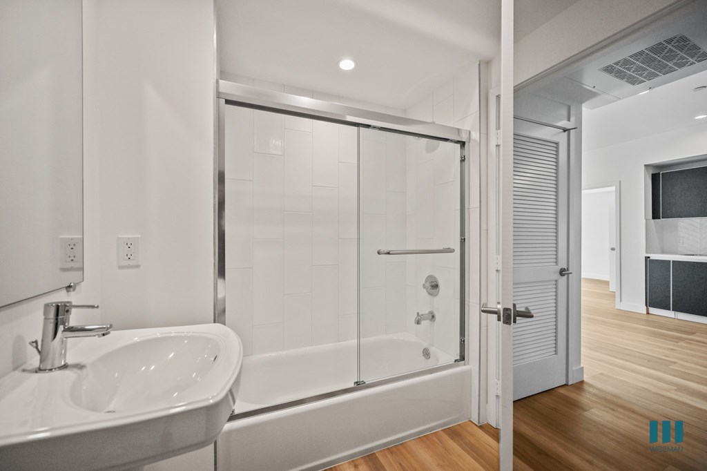 A white bathroom with a sink, mirror, and shower.