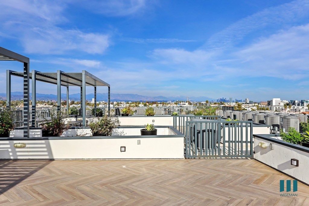 A rooftop patio with a wooden floor and metal railings overlooks a cityscape.