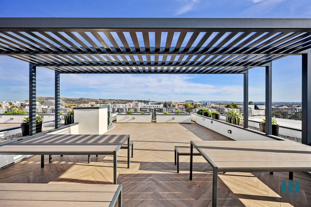 A rooftop patio with wooden floors and benches under a metal pergola.