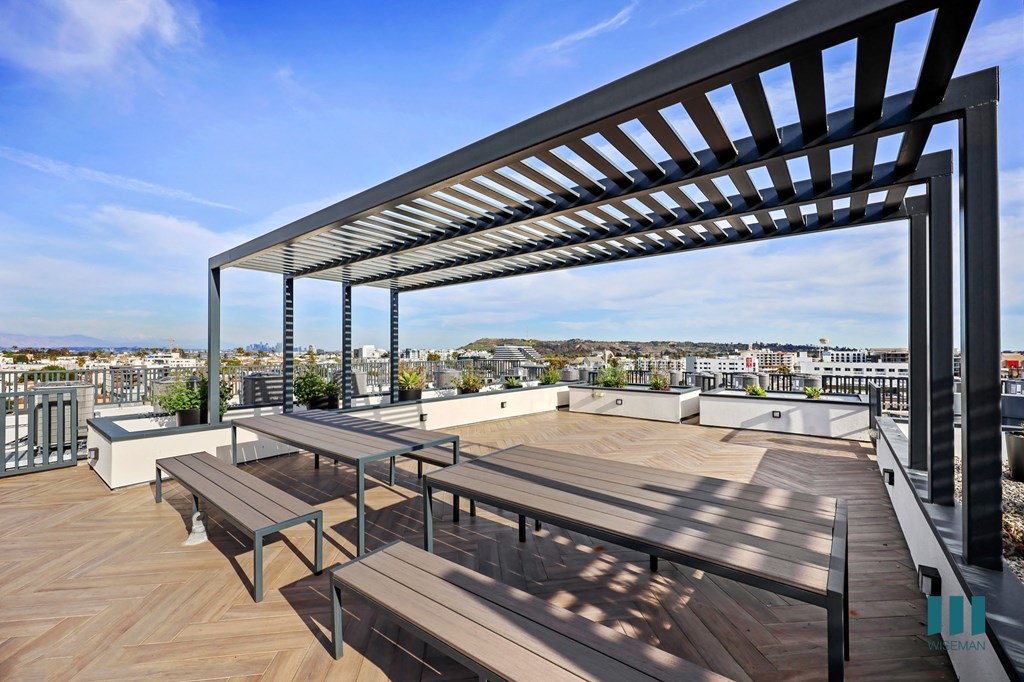 A wooden deck with a metal pergola and benches overlooking a cityscape.