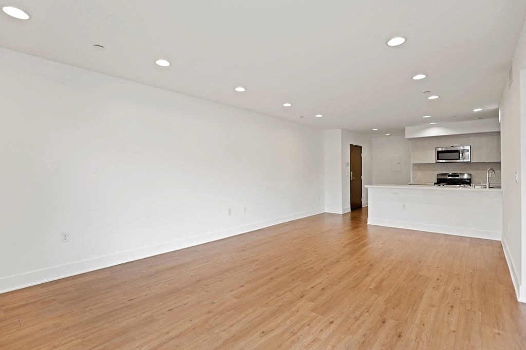 an empty living room with a kitchen in the background