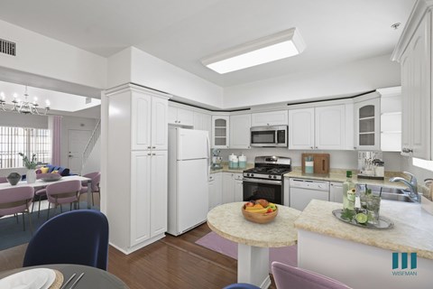 A kitchen with white cabinets and a table with a bowl of fruit on it.