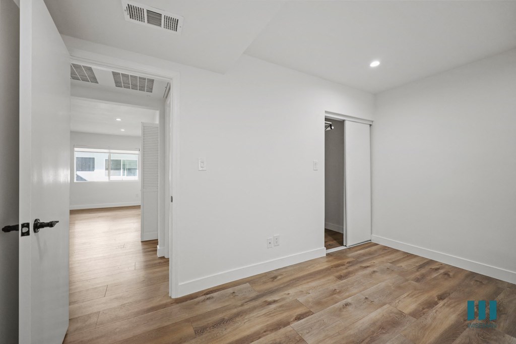 A room with white walls and wooden flooring, with a door on the left and a window on the right.