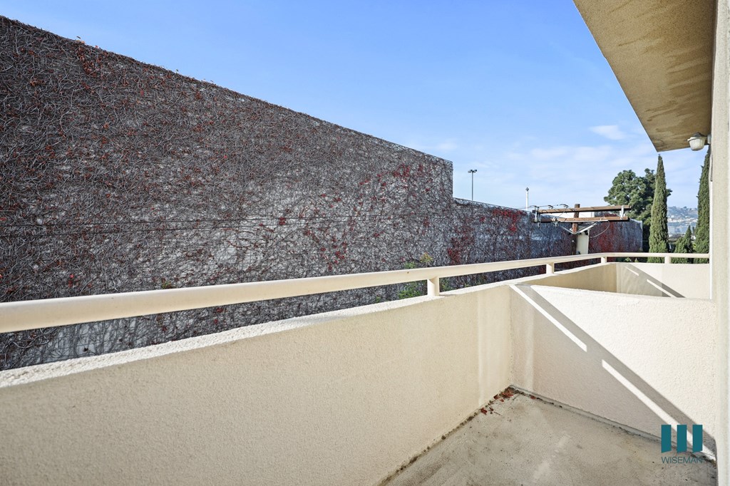 A balcony with a concrete floor and a wall covered in red vines.