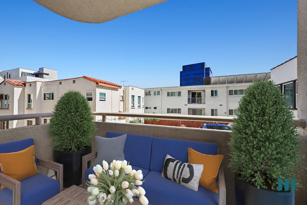 A blue couch with pillows and a vase of flowers on a balcony.