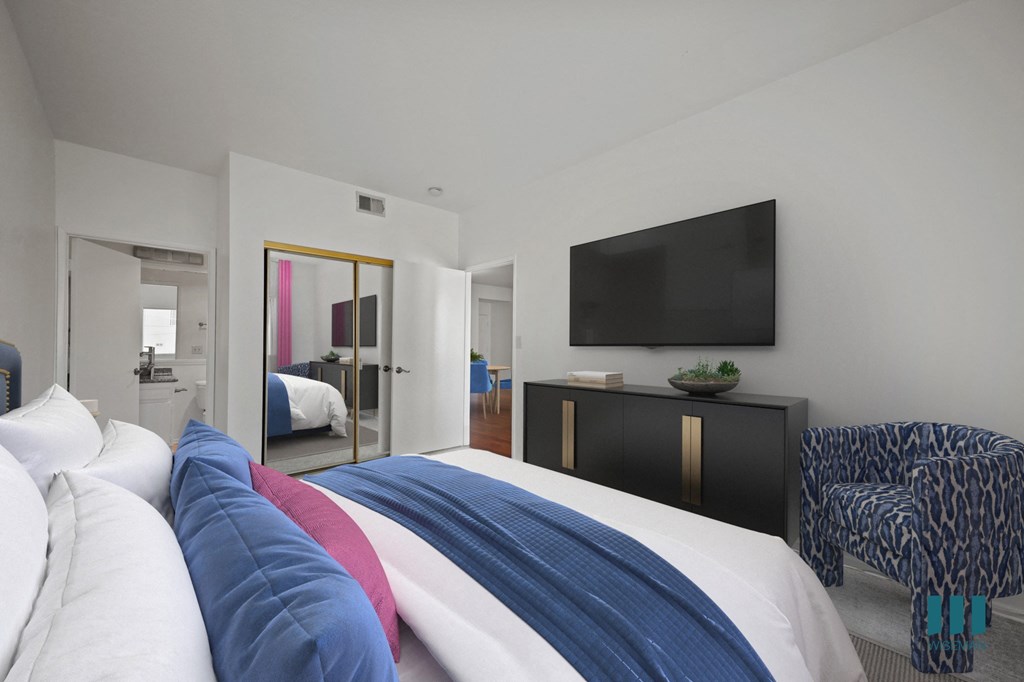 A bedroom with a bed covered in a white, blue and red comforter.
