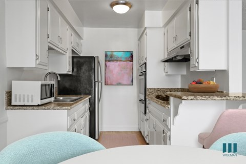A kitchen with white cabinets and a pink chair.