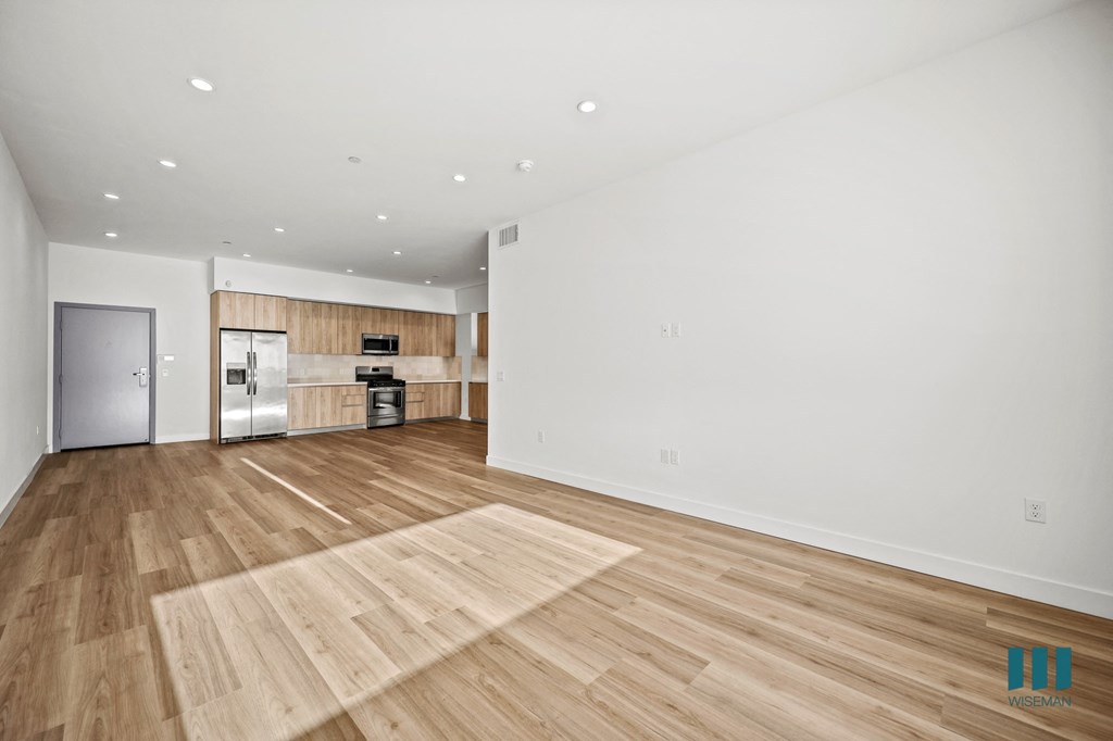 A spacious room with wooden flooring and a kitchen area in the background.