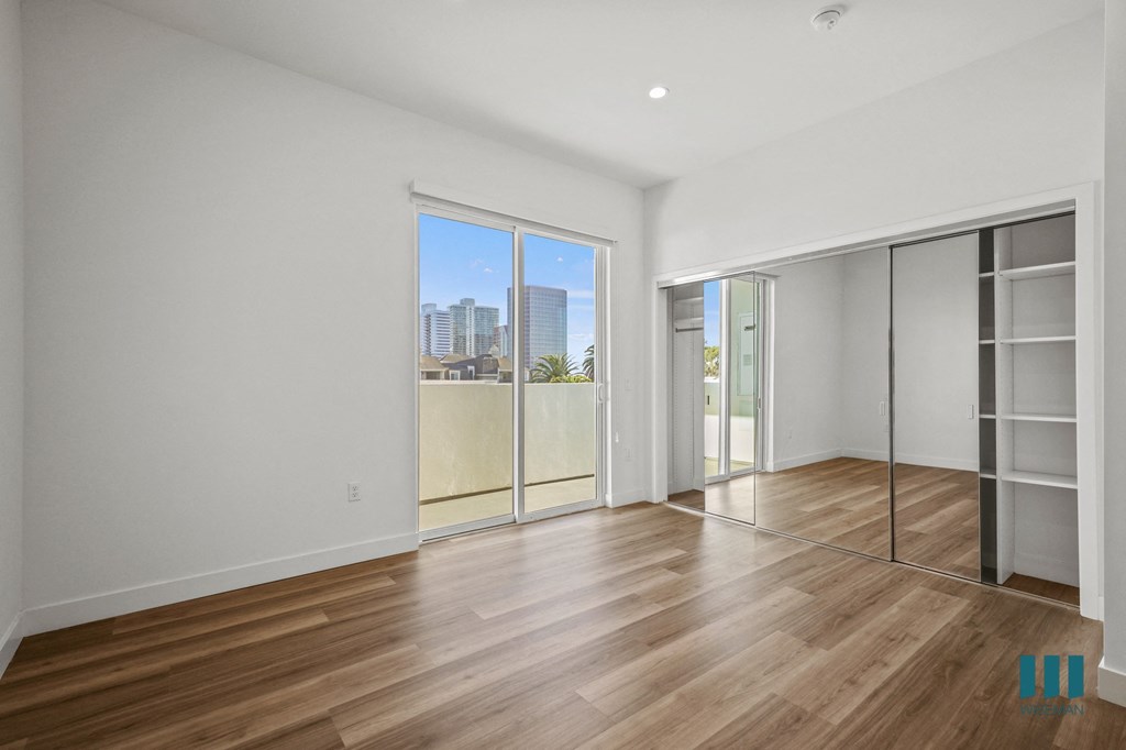 A spacious room with wooden flooring and a view of the city through a large window.