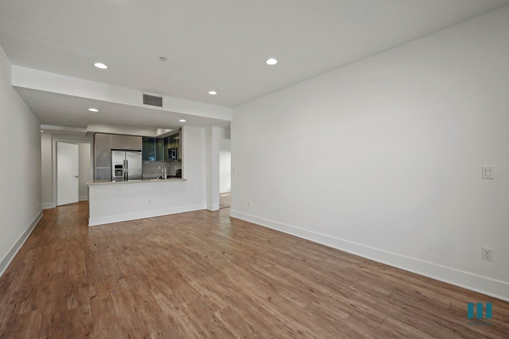 A large empty room with wooden floors and a kitchen area in the background.