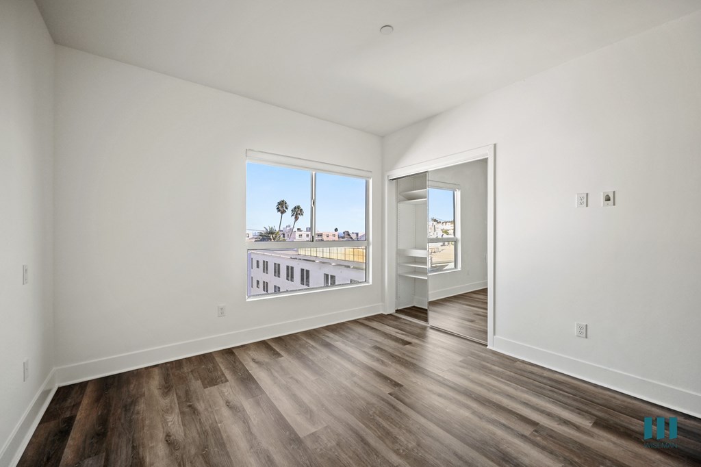A room with wooden floors and a view of a street with palm trees.