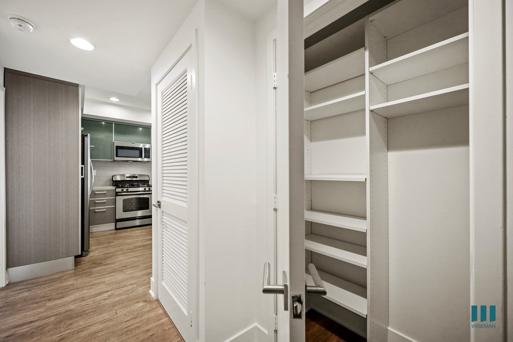A white door is open to a hallway with a kitchen in the background.