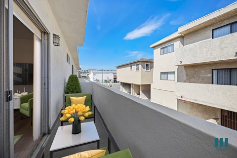 A balcony with a table and chairs overlooks a row of buildings.