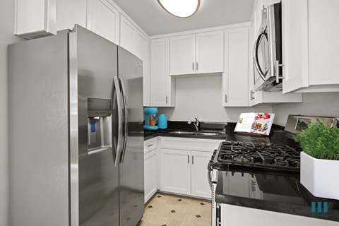 A modern kitchen with a stainless steel refrigerator and black countertops.