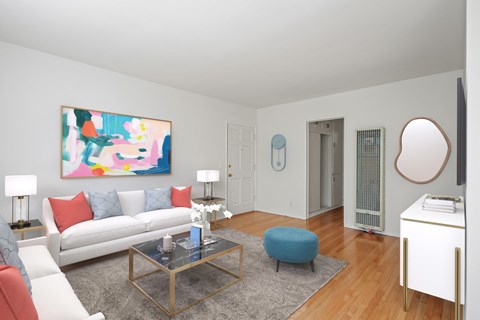 A living room with a white couch, a glass coffee table, and a painting on the wall.