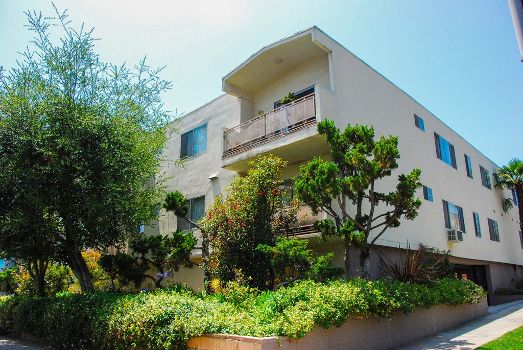 A white building with a balcony and a tree in front.