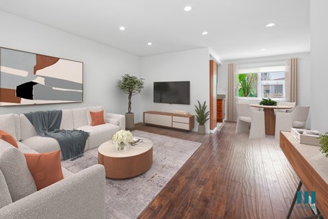 A modern living room with a grey sofa, orange pillows, a wooden coffee table, and a TV on the wall.