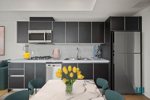 A modern kitchen with a table set for two and a vase of yellow flowers.