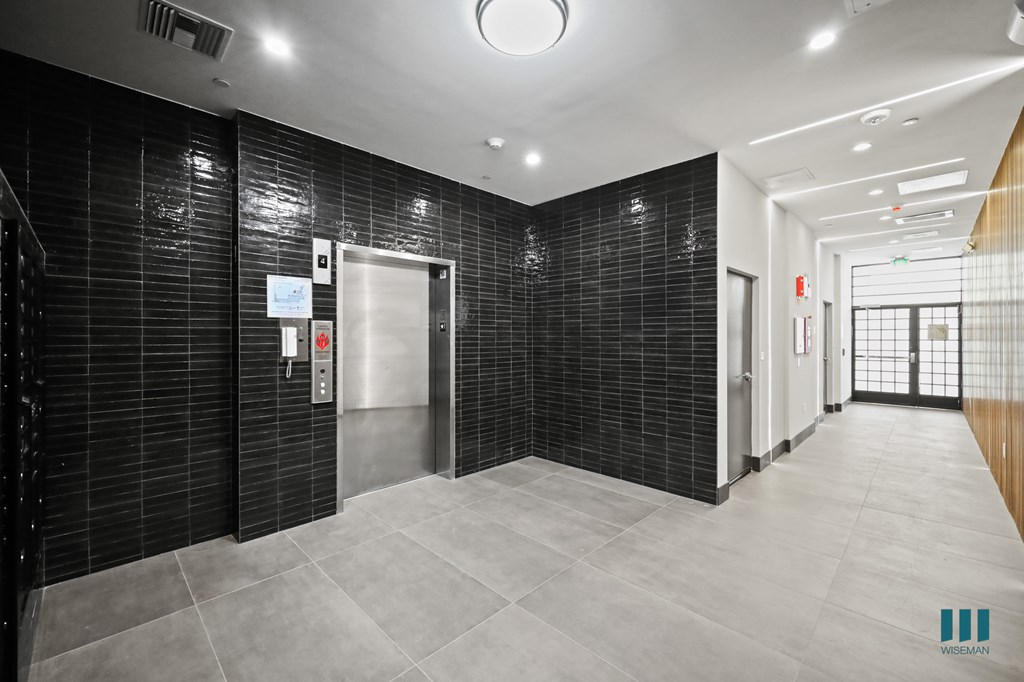 A hallway with a metal elevator doors and tiled walls.