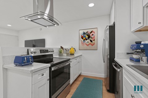 a kitchen with white cabinets and black appliances and a blue rug