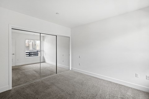 a living room with white walls and carpet and a mirrored door