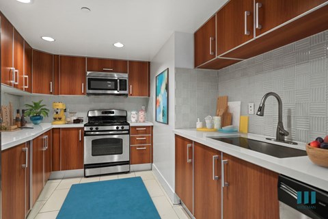 A kitchen with wooden cabinets and a blue rug on the floor.