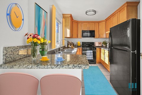 A kitchen with a black fridge, pink chairs and a clock on the wall.