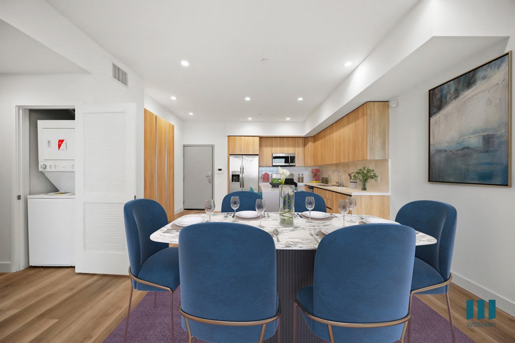 a long dining table with blue chairs in a room with white walls and wooden floors