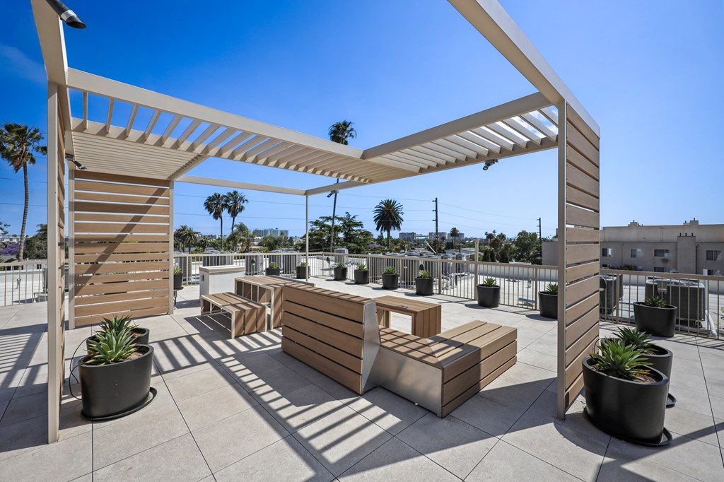 A sunny day on a rooftop patio with wooden furniture and a white pergola.